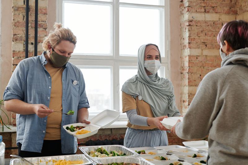 Volunteers serving plates of fresh food to a guest at a community meal