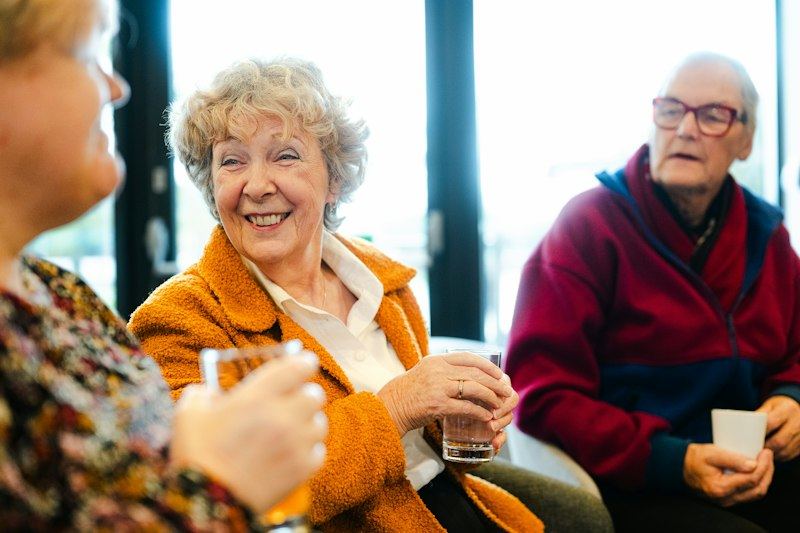 Three smiling older adults chatting together over drinks